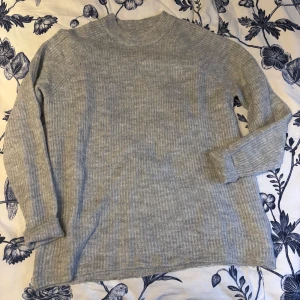 Grå ribbad tröja - Säljer en stilren grå ribbad tröja med långa ärmar. Perfekt för kyligare dagar och lätt att matcha med olika outfits. Tröjan har en klassisk design som passar till många tillfällen.