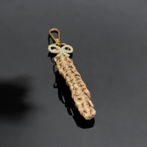 Guld nyckelring med pärldetalj - Elegant nyckelring i guldfärg med en flätad design och en dekorativ pärlrosett. Perfekt som accessoar för att ge en lyxig touch till dina nycklar eller väska.
