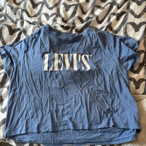 Blå t-shirt från Levi's - Säljer en blå t-shirt från Levi's med stort vitt tryck på framsidan. T-shirten har en avslappnad passform och korta ärmar. Perfekt för en casual look.