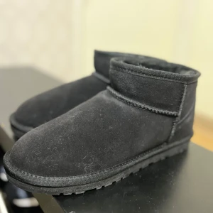 Svarta boots från UGG - Säljer ett par svarta UGG boots i mocka. De har en robust sula och är perfekta för kyligare väder. Klassisk design med UGG-logga på hälen. Perfekta för att hålla fötterna varma och bekväma.