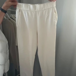 Vita byxor från Massimo Dutti - Snygga vita byxor från Massimo Dutti med elastisk midja för extra komfort. Byxorna har en stilren design med fickor fram och bak, vilket ger en elegant look. Perfekta för en chic och avslappnad stil.