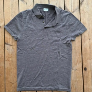 Grå/brun pikétröja från John Henric - Snygg grå pikétröja från Oscar Jacobson med klassisk krage och knappar framtill. Perfekt för en stilren look. Kortärmad och i ett mjukt material som känns skönt mot huden.