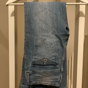 Blå jeans med flared ben från H&M - Snygga blå jeans från H&M med flared ben och justerbar midja. De har en praktisk ficka med knappdetalj på baksidan. Perfekta för en avslappnad stil.
