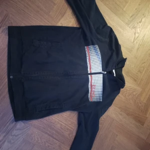  Hugo Boss  - Säljer en stilren svart hoodie/kofta från Hugo Boss med dragkedja och ett coolt rutigt mönster i rött och vitt på bröstet. Pris kan diskuteras säljer för att jag ej andvänder den längre