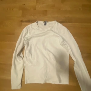 Vit långärmad tröja - Säljer en enkel och stilren vit långärmad tröja. Perfekt för lager på lager eller att bära som den är. Tröjan har en klassisk rund hals och är tillverkad i ett mjukt material för extra komfort.
