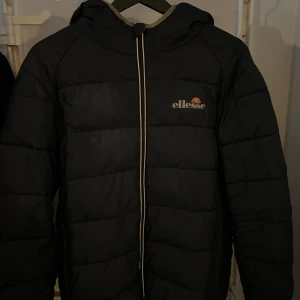 Svart pufferjacka från Ellesse - Säljer en blå pufferjacka från Ellesse med huva och dragkedja. Den är i gott skick och inga synliga slitage.