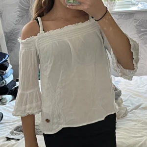 Vit offshoulder blus med spetsdetaljer - Säljer en söt vit offshoulder blus med spetsdetaljer och trekvartsärmar. Blusen har en luftig passform och är perfekt för varmare dagar. Den har också smala axelband för extra stöd. Kostade 200 kr när jag köpte den. Använd runt 5 gånger. Så himla fin och superskön