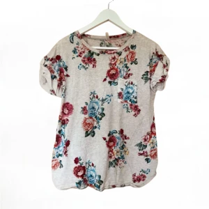 Blommig t-shirt från Intimissimi - Säljer en söt blommig t-shirt från Intimissimi i ljusgrått med färgglada blommor i rött, blått och grönt. T-shirten har korta ärmar och en rund halsringning. Perfekt för en avslappnad stil. 