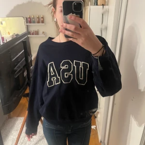 Mörkblå tröja med USA-tryck från Ralph Lauren - Säljer en snygg mörkblå tröja från Ralph Lauren med stort USA-tryck på framsidan. Tröjan har långa ärmar och en avslappnad passform. I tröjan står det att det är storlek L men tycker den är alldeles för liten för det och skulle påstå att den är mer som M/S