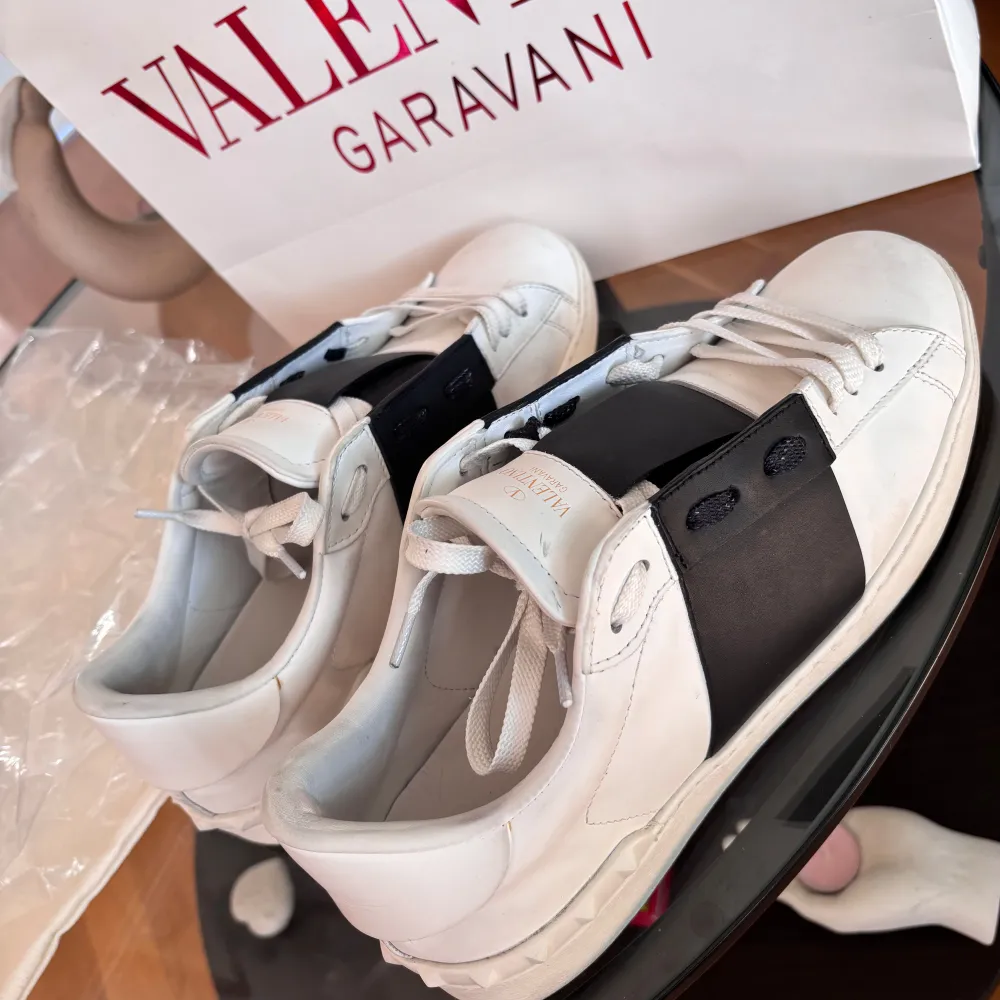 Säljer ett par snygga Valentino Garavani sneakers i vitt med en bred svart rem över. Skorna är i skinn och har en stilren design med snörning. Perfekta för både vardag och fest!🎉 Kom privat för övriga frågor. Skor.