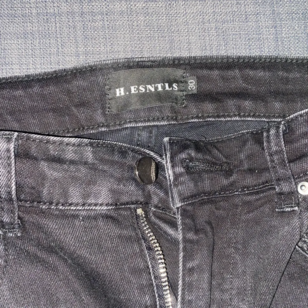 Säljer ett par svarta jeans från H.ESNTLS i storlek 30. De har coola slitningar med färgglada detaljer under, vilket ger dem en unik look. Perfekta för en avslappnad och trendig stil. Dragkedja och knapp framtill.. Jeans & Byxor.