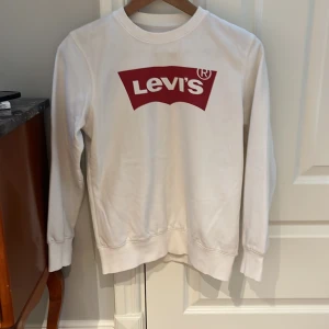 Vit Levis sweatshirt - Levis logan på framsidan är lite sliten men annars mycket bra skick. Storlek 164 eller 14 år men sitter lite litet i storleken. Ett lite tunnare material lagom till sommar kvällar i 70% bomull och 30% polyester.