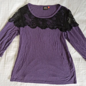 Lila topp med spetsdetaljer från ONLY - Säljer en superfin lila topp från ONLY i storlek S. Den har snygga svarta spetsdetaljer över axlarna och bröstet som ger en elegant touch. Toppen har trekvartsärm. Materialet är mjukt och bekvämt. Pris är självklart förhandlingsbart!
