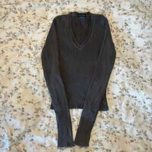 Grå ribbad tröja från Brandy Melville  - Säljer en stilren grå ribbad tröja från Brandy Melville med v-ringad hals. Tröjan har långa ärmar och är perfekt för kyligare dagar. Passar bra till både jeans och kjol.