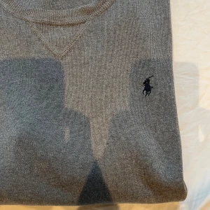Ralph Lauren knit - Säljer en skön grå knit från Ralph Lauren. Tröjan har en broderad logotyp på bröstet och ribbade muddar vid ärmslut och nederkant. Riktigt skön passform och jättebra skick. Tagen i nacken har rivits av men tröjan är äkta och resterande tags sitter kvar.