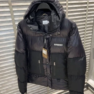 Svart dunjacka från Burberry - Snygg svart dunjacka från Burberry med huva och dragkedja. Jackan har Burberry-logga på bröstet och ryggen, samt praktiska fickor med knappar. Perfekt för kyliga dagar.