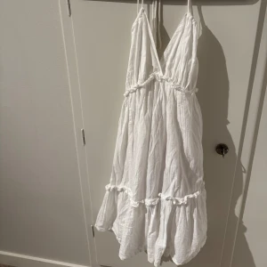 Vit sommarklänning med volanger - Charmig vit klänning med smala axelband och volangdetaljer. Perfekt för varma sommardagar med sin luftiga design och omlott-look. Klänningen har en v-ringad hals och är tillverkad i ett lätt material. Passar mer XS/S enligt mig då jag själv har det och den passar mig, men tyvärr inte kommer till användning💕