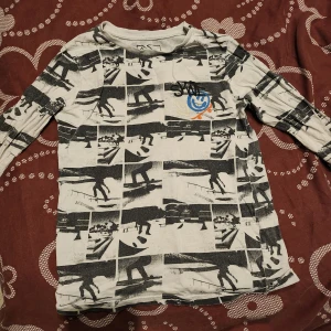 Svartvit långärmad tröja med grafiskt mönster - Säljer en cool svartvit långärmad tröja med ett unikt grafiskt mönster och en färgglad detalj på bröstet. Perfekt för den som vill sticka ut med en stilren look.