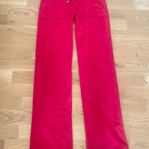 Juicy Röda mjukisbyxor med fickdetaljer - Snygga röda mjukisbyxor med praktiska fickor och snörning i midjan. Perfekta för en avslappnad stil med en touch av färg. Broderad detalj på fickan ger en extra stilpoäng. Storlek XS