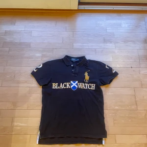 Chief keef type pike Polo ralph lauren Blackwatch sällsynt vintage - Säljer en snygg svart pikétröja från Ralph Lauren med 'Black Watch' broderat i guld framtill. Tröjan har en klassisk krage och korta ärmar, perfekt för en stilren look. En av de ända äkta tröjorna av denna modell du någonsin kommer hitta. Skickar samma dag 📦