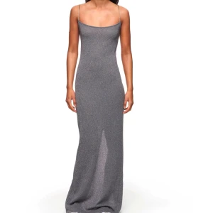 Glittrig långklänning med  - Glittrig långklänning i silver med smala axelband och öppen rygg. Klänningen har en figurnära passform och korsade band i ryggen för en stilfull look. Passar bra till nyår. Helt ny med prislapp, hann inte returnera i tid. 