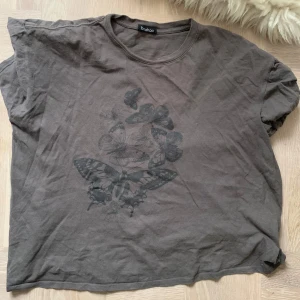 Grå t-shirt med fjärilstryck från Boohoo - Snygg grå t-shirt från Boohoo med ett coolt fjärilstryck på framsidan. Perfekt för en avslappnad stil. T-shirten har korta ärmar och en rund halsringning.