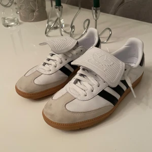 Adidas Samba sneakers - Snygga Adidas Samba sneakers i vitt och svart med klassiska tre ränder. Skorna har en gummisula och snörning. Perfekta för en sportig look.