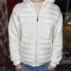 Vit quiltad jacka med huva - Snygg vit quiltad jacka/cardigan med dragkedja och huva, perfekt för mildare dagar, den har även praktiska fickor med dragkedja. Säljer för att den inte kommer till användning. Den är som ny och har inga defekter alls. Storlek S, hör av er vid intresse eller frågor💕