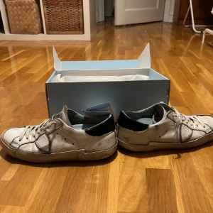 Philippe Model Skor - Snygga vita sneakers från Philippe Model med svarta detaljer och snörning. Perfekta för en avslappnad stil. Skorna kommer i originalkartong. Lite slitna men nästan allt går och laga med lite sko lim. Sulan i skon är ganska sliten fram vid tårna så jag skickar med ett par extra sulor.