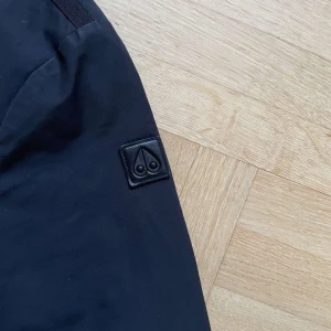 Svart jacka från Moose Knuckles - Snygg svart jacka från Moose Knuckles med diskret logga på ärmen. Storlek S.