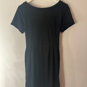 Svart klänning  - Svart klänning med spetsdetalj i nederkant. Klänningen har ett band baktill som man kan knyta rosett och en rosett i nacken. Storlek M.