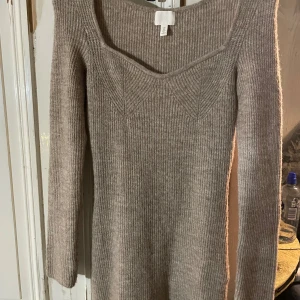 Beige stickad klänning från H&M - Säljer en mysig beige stickad Klänning från H&M. Klänningen har en v-ringad design och långa ärmar, perfekt för kyligare dagar. Den ribbade strukturen ger en stilren look. Passar bra till både strumpbyxor och kjol.