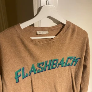 Beige tröja med text från Sandro - Snygg beige tröja från Sandro med texten 'FLASHBACK' i grönt på framsidan. Passar xxs-m. 91% ylle och 9% Kashmir 
