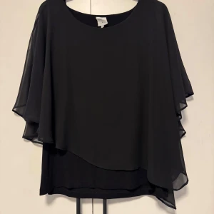 Svart blus från Pearl - Elegant svart blus från Pearl med flödande lager och kortärmad design. Perfekt för en stilren look med en luftig känsla. Passar bra till både jeans och kjol.