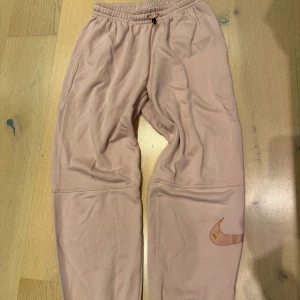 Rosa joggers från Nike strl S - Supersköna rosa mjukisbyxor från Nike. Byxorna har resår i midjan och en diskret Nike-logga på benet. Loose fit strl S. Knappt använda. Nypris 699kr.
