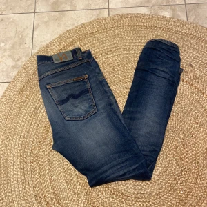 Blå jeans från Nudie Jeans - Snygga blå jeans från Nudie Jeans med klassisk femficksdesign och orange sömmar. Perfekta för en avslappnad stil med en modern touch. Modellen heter grim Tim och sitter slim fit. Bara att höra av er om ni har frågor!