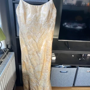 Gul långklänning från LaBelle Fashions - Elegant gul långklänning i 100% silke från LaBelle Fashions. Klänningen har ett vackert blommigt mönster och en mjuk, skimrande yta. Perfekt för speciella tillfällen med sin klassiska och tidlösa design.