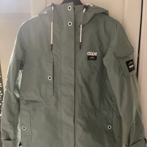 Grön jacka från Dope - Snygg grön skidjacka från Dope med justerbar huva och flera praktiska fickor. Jackan har långa ärmar och en stilren design med logotypdetaljer på bröstet och ärmen. Använd en vinter säsong men är i väldigt bra skick💚jackan är i storlek XS men skulle säga att den passar S också. 