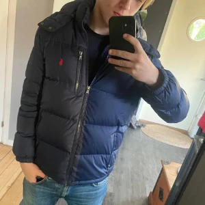 Polo Ralph Lauren dunjacka - Säljer en snygg mörkblå dunjacka från Polo Ralph Lauren. Jackan har en avtagbar huva och praktiska dragkedjefickor. Jackan är i mycket bra skick. Modellen är ca 176-177cm lång. Jackan är i storlek XL i barnstorlek vilket motsvarar XS-S i herrsortlek. (Passar dig som är ca 165-180) Teveka inte att höra av dig om du har någon fråga.