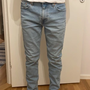 Ljusblå jeans från Levi's - Säljer ett par ljusblå Levi's jeans med klassisk femficksdesign och knappgylf. De har en slim passform och är perfekta för en avslappnad stil. Levi's logga syns tydligt på bakfickan.
