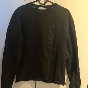 Svart långärmad tröja från Calvin Klein - Säljer en stilren svart långärmad tröja från Calvin Klein med diskret logga på framsidan. Perfekt för en avslappnad look.
