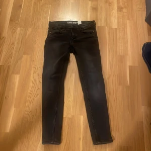 Svarta Super Stretch jeans - Säljer ett par svarta Super Stretch jeans i skinny fit. De har en klassisk femficksdesign och är tillverkade i stretchigt denim för extra komfort. Perfekta för en stilren look.