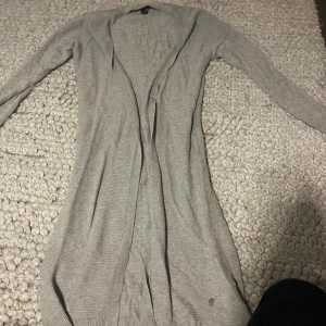 Grå kofta från Esmara - Säljer en stilren grå kofta från Esmara. Den är lång och har långa ärmar, perfekt för lager-på-lager under kyligare dagar. Koftan är i ett mjukt material som ger en bekväm passform.