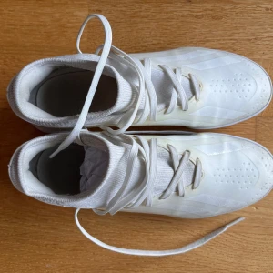 Vita fotbollsskor inomhus från Adidas - Snygga vita fotbollsskor från Adidas med snörning och låg profil. Perfekta för inomhusspel med en slitstark sula och diskret design. Använda en säsong. Kan hämtas i Årstaberg Stockholm.