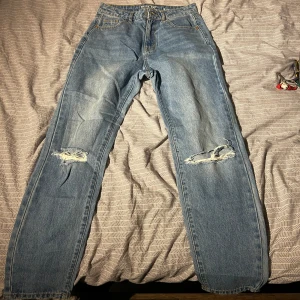 Blå jeans från Noisy May - Säljer ett par blå jeans från Noisy May med slitna detaljer på knäna. De har en klassisk femficksdesign och knappgylf. Perfekta för en avslappnad stil.