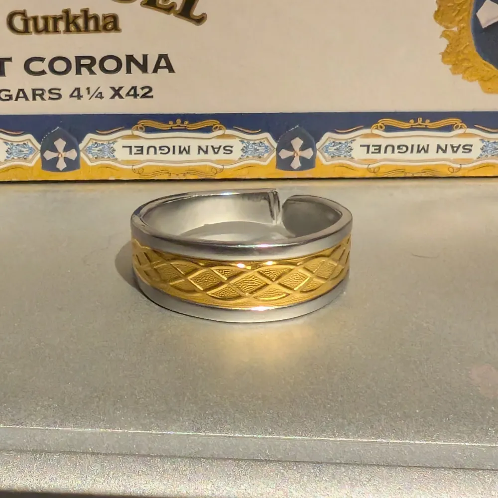 Elegant ring i silver med ett detaljerat guldfärgat mönster. Perfekt för att ge en touch av lyx till din stil. Omkrets 67mm (L/XL) . Asusteet.