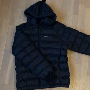 PeakPerformance Tomic Insulated Hood Jacket  - Säljer en mörkblå dunjacka från Peak Performance. Jackan är i väldigt bar skick, perfekt för kyliga dagar.