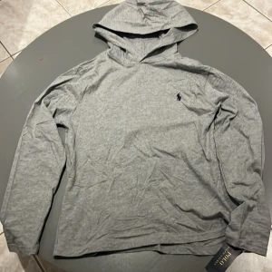 Grå hoodie från Polo Ralph Lauren - Snygg grå hoodie från Polo Ralph Lauren med det klassiska blå logotypen på bröstet. Perfekt för er som vill hoppa på trenden med unika ralph lauren hoodies nu i vinter.   Hoodies är i storlek xs = största barn storlek.Helt oanvänd då den var för liten för mig som e 185. 10/10 kondition. Pris kan diskuteras vid snabb affär