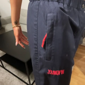 Mörkblå byxor med röd detalj - Snygga mörkblå byxor med röd broderad text och detaljer. Byxorna har en loose passform och hög midja med knappar. 