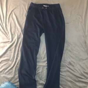 Mörkblå konstymbyxor med dragsko - Säljer ett par mörkblå mjukisbyxor med elastisk midja och dragsko. Perfekta för en avslappnad stil. Byxorna har en enkel design och är gjorda i ett mjukt material för extra komfort.